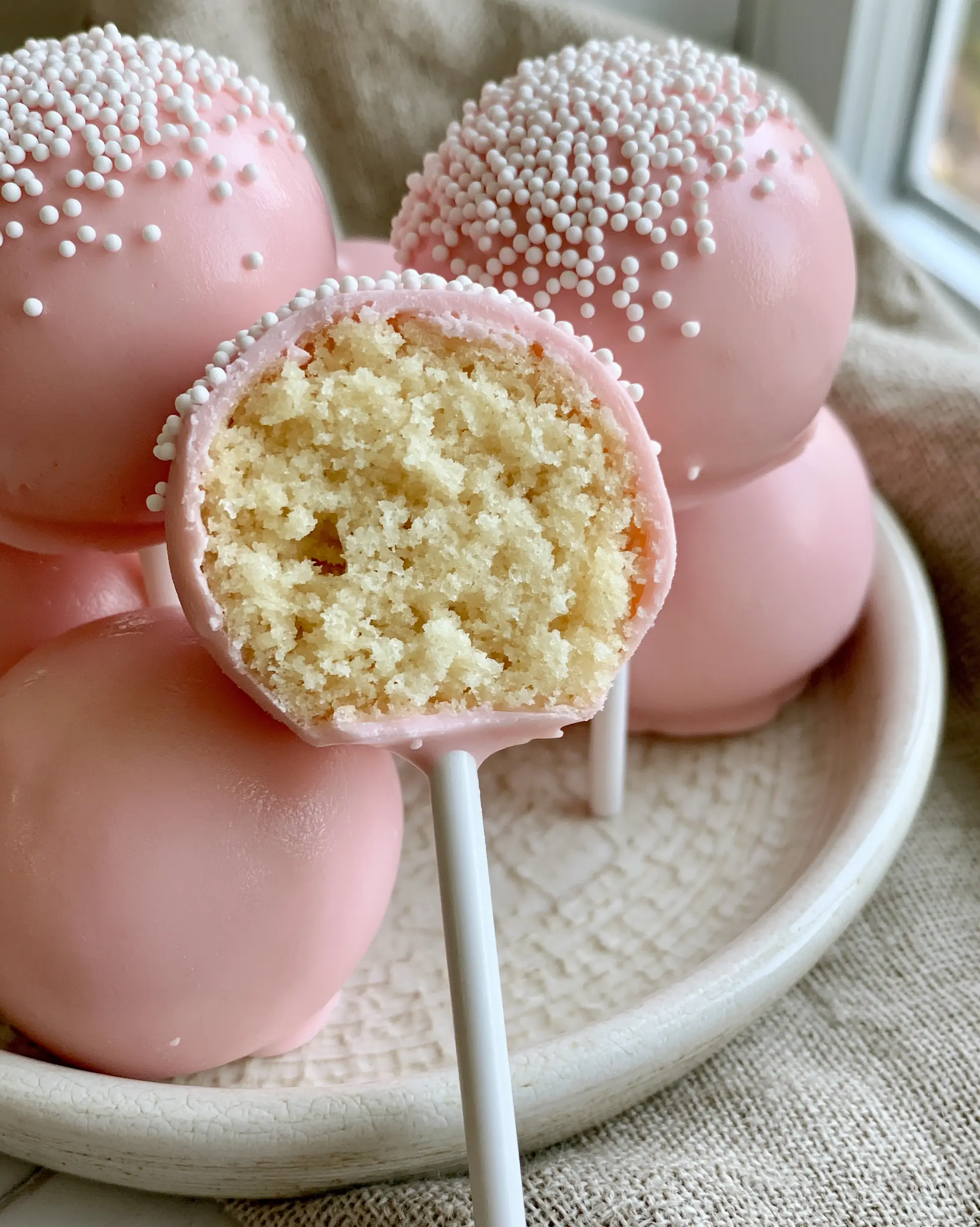 Close-up of a pink cake pop with a bite taken out, revealing a dense pale-yellow vanilla crumb. (cake pop recipes)