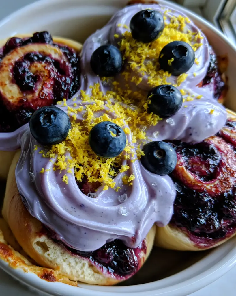 Blueberry Cinnamon Rolls with Lavender Cream Cheese Frosting and Lemon Zest 2 Macro top-down view of six pull-apart blueberry cinnamon rolls in a white ceramic dish with pale lavender frosting. (blueberry cinnamon rolls)