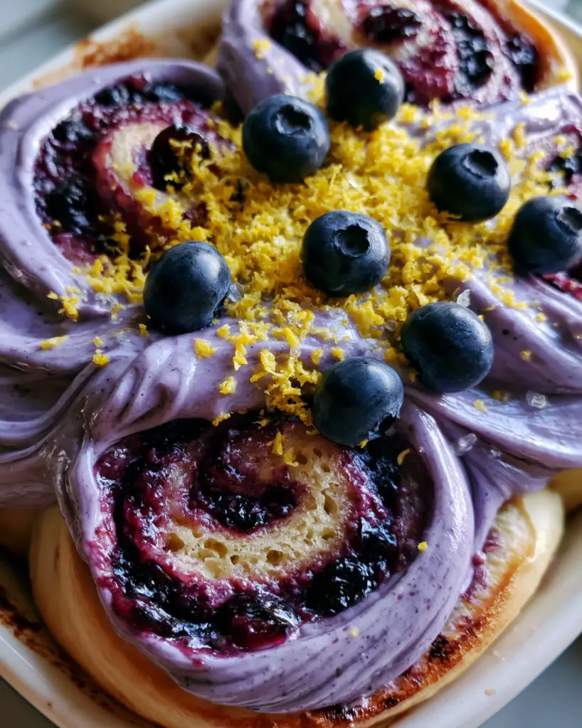 Blueberry Cinnamon Rolls with Lavender Cream Cheese Frosting and Lemon Zest 1 Close-up of glossy lavender frosting swirls on blueberry cinnamon rolls with lemon zest and sugar crystals. (blueberry cinnamon rolls)