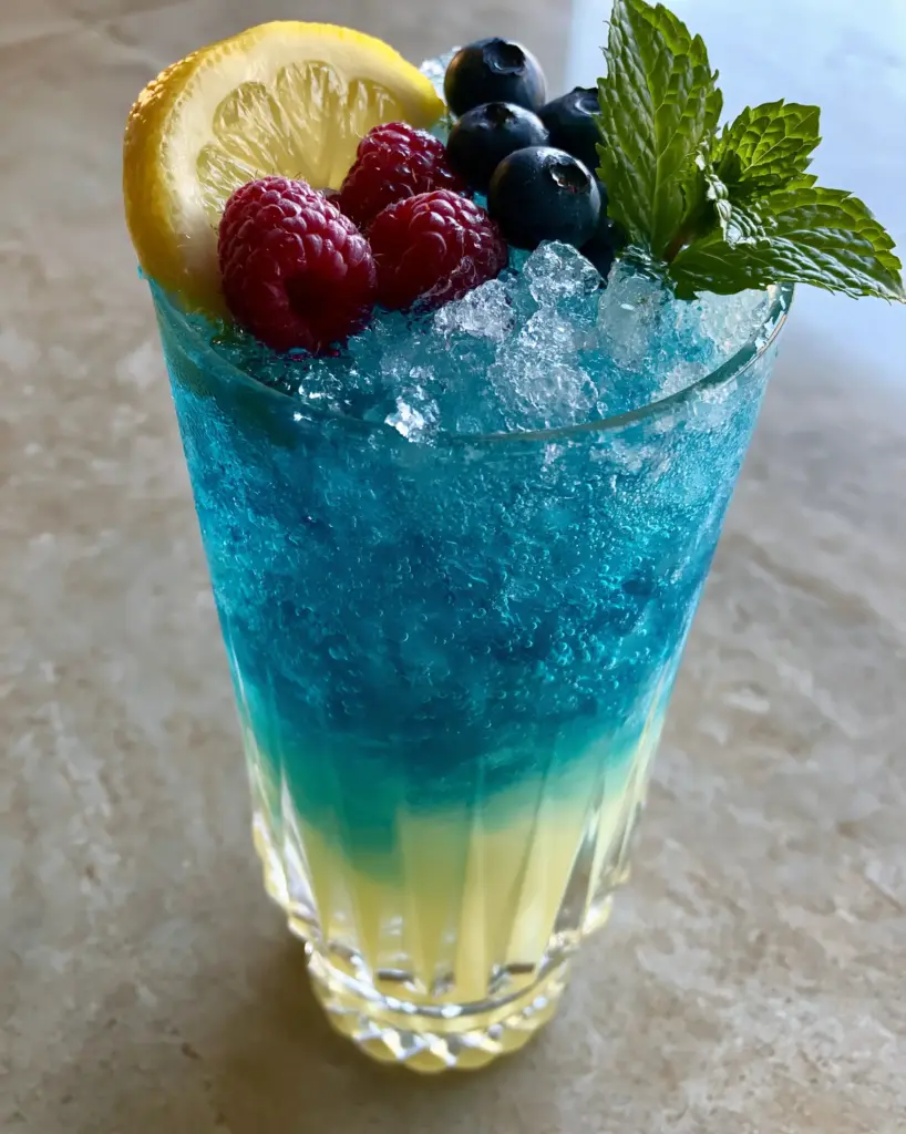 Blue Raspberry Lemonade Recipe: A Naturally Electric Summer Refreshment 2 Side view of a blue raspberry lemonade in a ribbed glass showing the yellow to blue ombré transition. (blue raspberry lemonade)