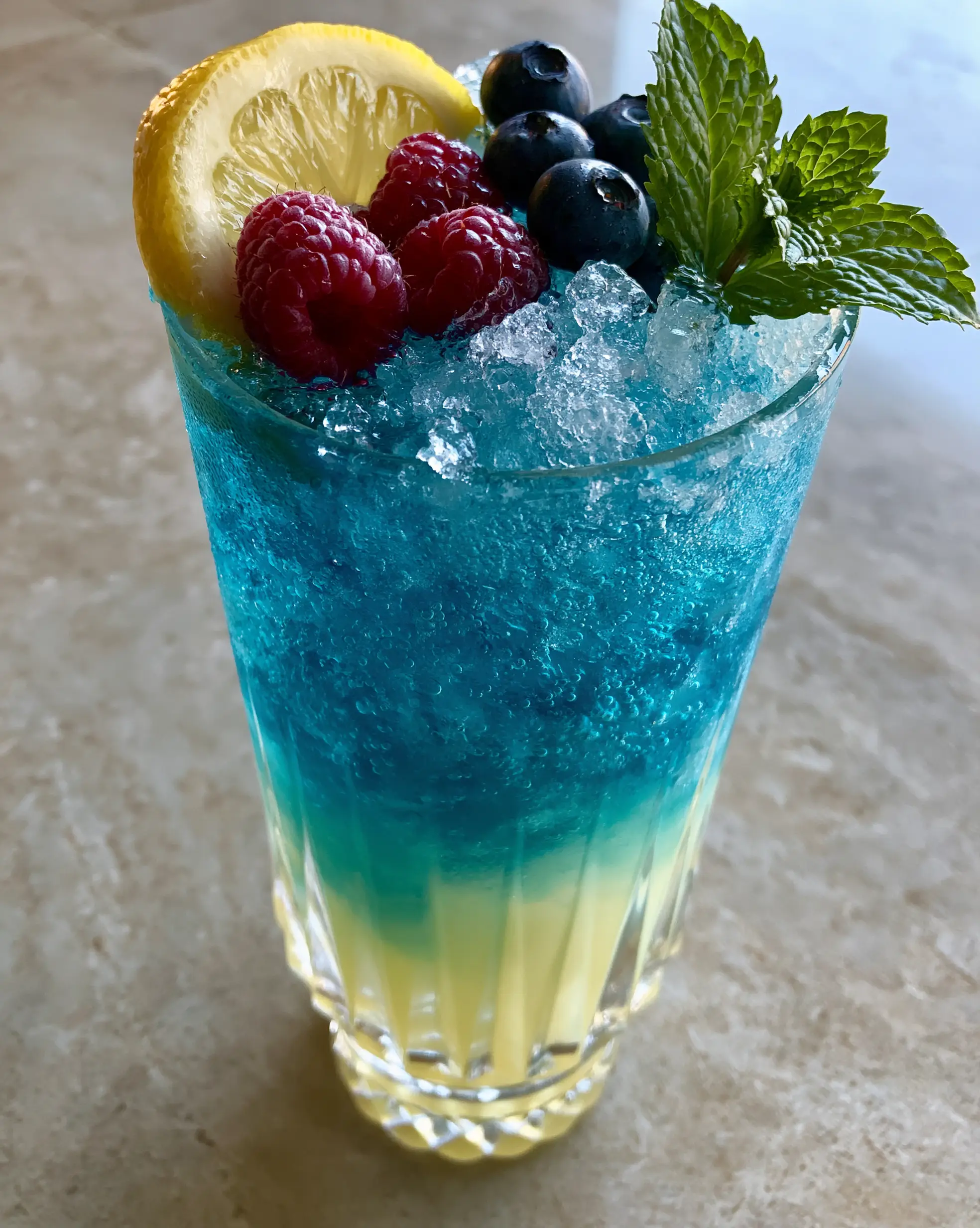 Blue Raspberry Lemonade Recipe: A Naturally Electric Summer Refreshment 4 Side view of a blue raspberry lemonade in a ribbed glass showing the yellow to blue ombré transition. (blue raspberry lemonade)
