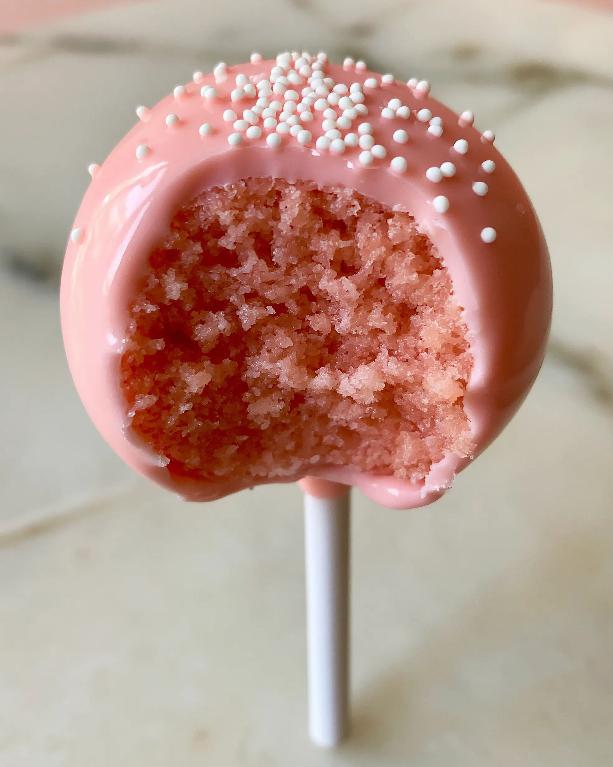 Close-up of a bitten cake pop revealing a dense pastel pink vanilla crumb. (cake pop flavors)