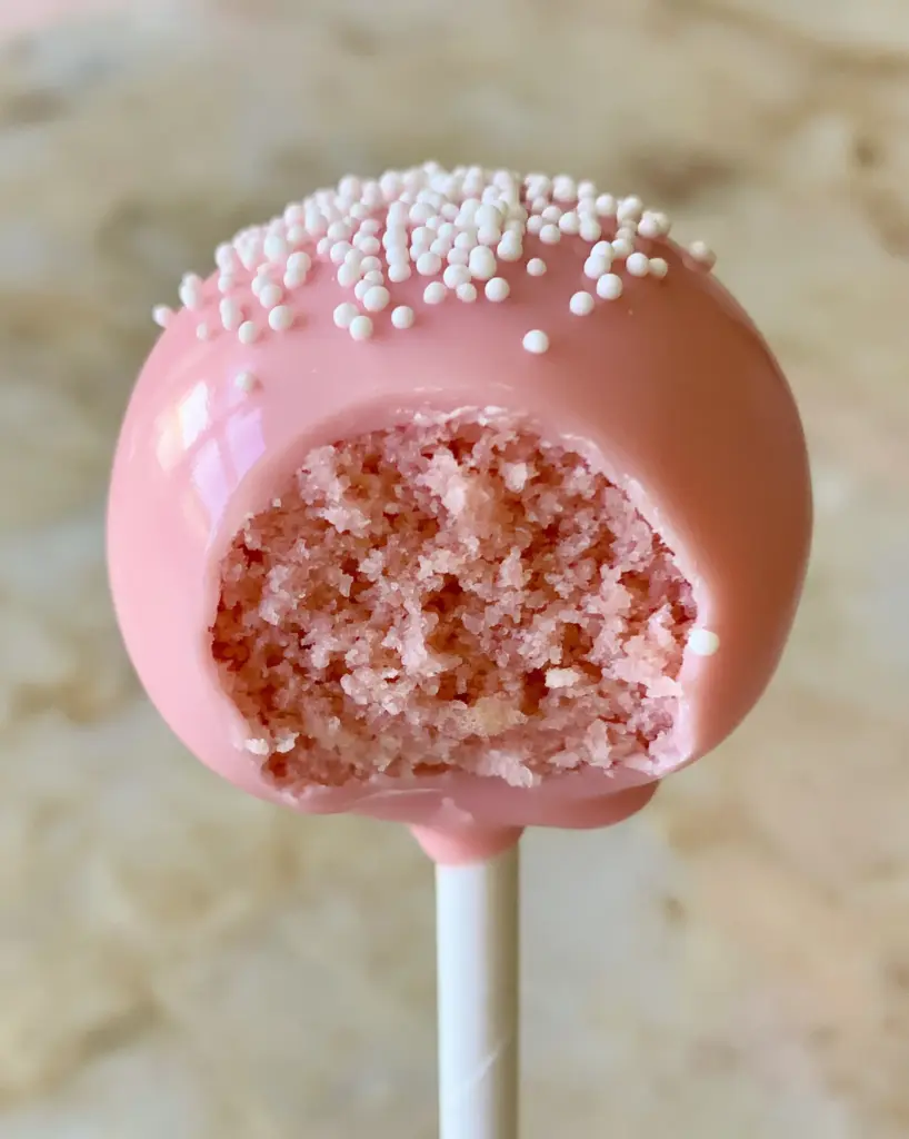 A glossy pink cake pop held against a neutral marble background. (cake pop flavors)